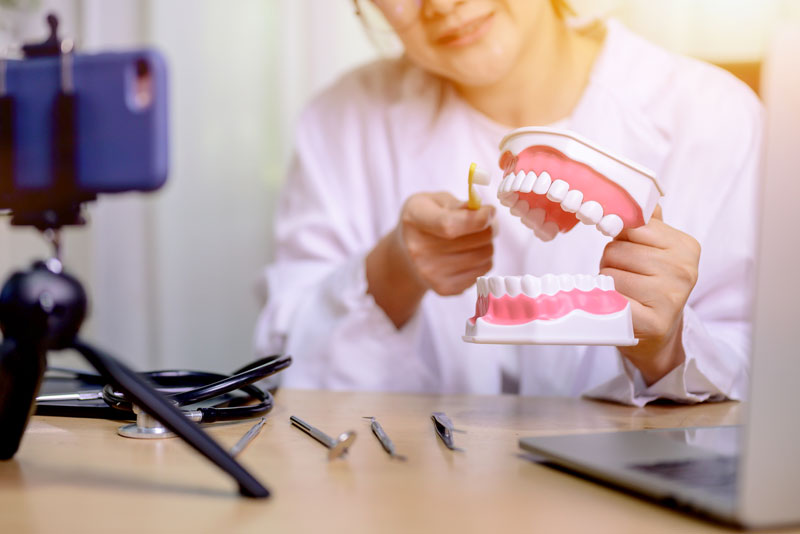 a dentist holidng a mouth model and toothbrush making stock blog content.